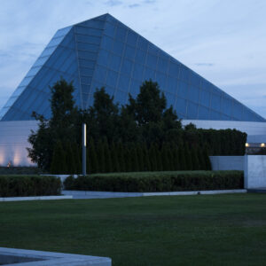 a blue glass building that is shaped like a triangle. it has trees and grass in front of it