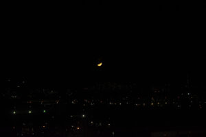a night with a crescent yellow moon and building lights.