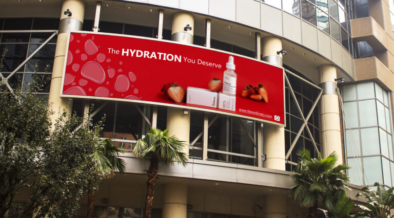 a billboard that shows the ordinary hyaluronic acid product. the product is surrounded by strawberries on a red background.